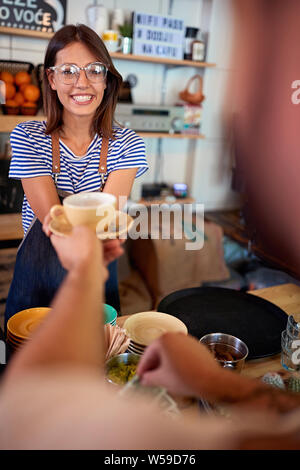 Smiling waitress in cafe serving customer with coffee. Stock Photo