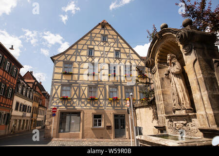 A traditional house (Bauernhaus or farmhouse) and the water fountain outside the Elisabethenkirche in the Bavarian city of Bamberg, Germany. Stock Photo