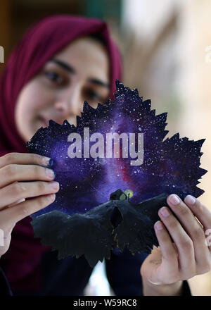 (190727) -- BEIJING, July 27, 2019 (Xinhua) -- Leen Alhaj displays a grape leaf drawn with a painting inside her house in Nuseirat refugees camp in the central Gaza Strip, July 22, 2019. Leen Alhaj, 21, based in Nuseirat refugees camp in the central Gaza Strip, is drawing on grape leaves and turning them into beautiful paintings. Alhaj, a student in psychological department at the Islamic University of Gaza, imitates the nature by her art paintings, such as the sky at night adorned by stars and the moon, and the reflection of the sun at sunset on lakes, trees, waterfalls and other scenes. Stock Photo