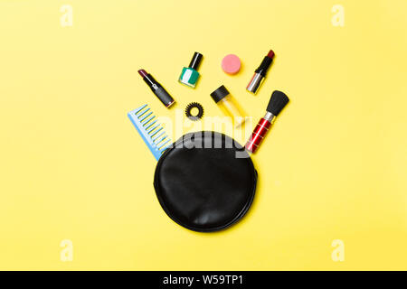 Top view od cosmetics bag with spilled out make up products on yellow background. Beauty concept with empty space for your design. Stock Photo