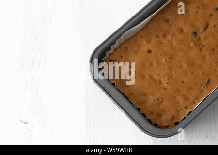 Fruit cake loaf mixture in a metal baking tin.  On a white wood background Stock Photo
