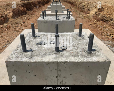 Row of reinforced concrete foundations with metal anchor bolts designed for the installation of metal columns. Foundations of warehouse on the constru Stock Photo