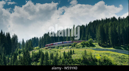 Arosa, GR / Switzerland - 24. July, 2019:  red Rhaetian railway train in a green summer mountain landscape in the Swiss Alps Stock Photo