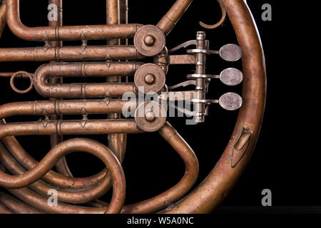 Vintage bronze pipes, valve, key mechanical elements french horn on black isolated background. Good pattern, prompt music instrument. Stock Photo