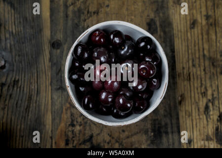 horizontal view of fresh organic ripe black cherries in a white bowl on a rustic wooden table Stock Photo