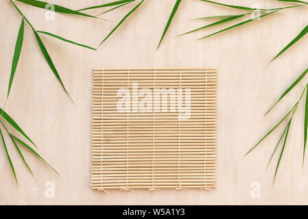 Green bamboo leaves and bamboo mat, asian style background, top view, copy space. Trendy bamboo leaves flat lay on white wooden background. Stock Photo