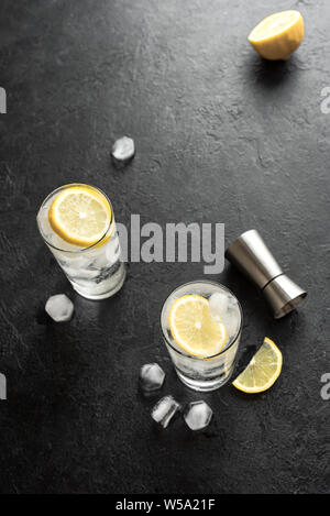 Alcohol drink (gin tonic cocktail, vodka cocktail, tom collins cocktail) with lemon and ice on rustic black stone table, copy space, top view. Iced so Stock Photo