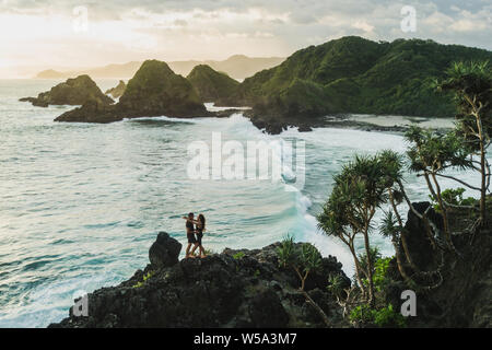 Man and woman looking to each other with love at sunset with amazing ocean and mountain view. Travel concept, panoramic shot, wanderlust. Stock Photo