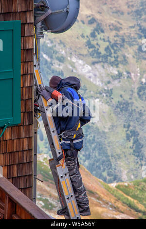 Worker with tools standing on the stairs at a wooden house in the mountains Stock Photo