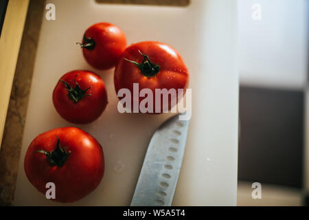 Freshly picked tomatoes from the garden in the kitchen on a plastic cutting board and near a chef knife Stock Photo
