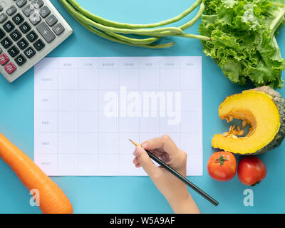 Calories control, meal plan, food diet and weight loss concept. top view of hand filling meal plan on blank paper with calculator and vegetable isolat Stock Photo