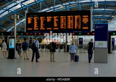 London, United Kingdom - July 23, 2019: Waterloo train station on weekday morning showing some motion blurring and commuters looking at information bo Stock Photo