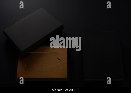 Slick black gift boxes with brown cardboard inside on black background Stock Photo
