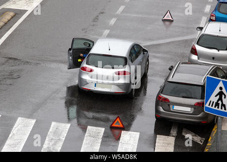 Scene of a broken down car on a city street road near a crosswalk with and a red triangle to warn other road users. Rainy day. Copy space Stock Photo
