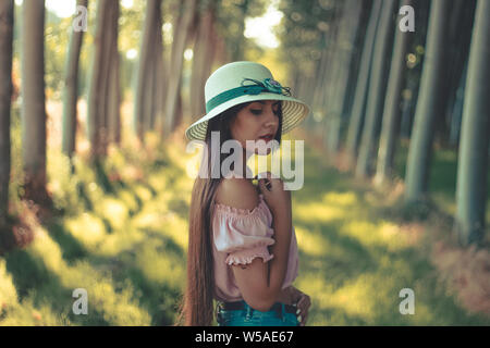 Pretty long haired brunette hispanic girl wearing white sun hat pink blouse and short blue jeans Stock Photo