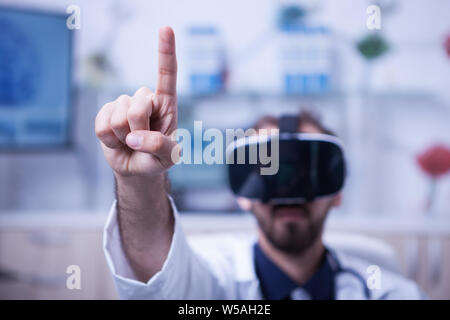 Close up of doctor pointing in the air with his finger wearing a virtual reality headset. Doctor in his medicine uniform. Stock Photo