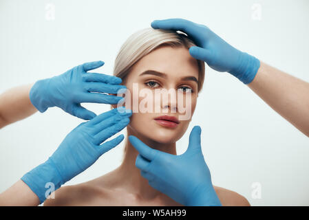 Facial surgery. Beautiful blonde woman waiting for facial surgery while surgeons in blue medical gloves examining her face. Plastic surgery concept. Healthcare. Beauty concept. Stock Photo