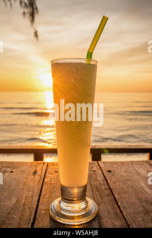 Fresh fruit juice with ice on wooden table at the tropical beach at sunset in Thailand Stock Photo