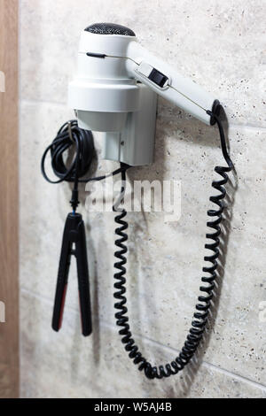 Tools for hair care electric hair dryer and curling iron hang on the wall of the toilet in the hotel. Stock Photo