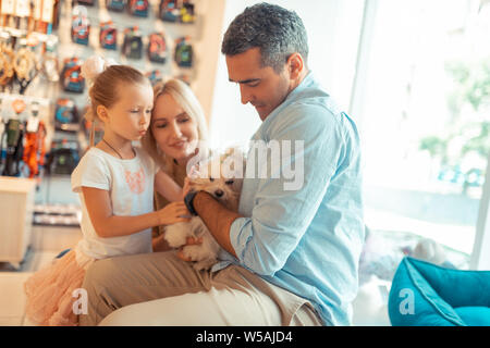 Parents and their cute girl taking fluffy white dog to the pet shop Stock Photo