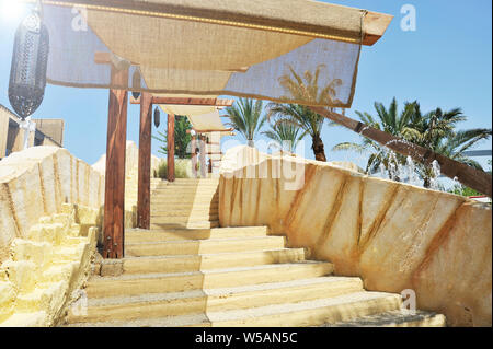 Outdoor stairway with a sun tent. In the background there are palm trees and fountain jets of water. A typical Arab lamp is hanging. Stock Photo