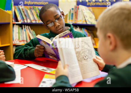 An Afro-Caribbean boy and a Caucasian boy reading in the library at a primary school in the UK. Stock Photo