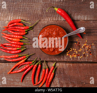 Hot chilli pepper sauce paste harissa, traditional Tunisia, Moroccan, Arabic cuisine adjika ,chili pepper spices and fresh red chilli peppers, over wo Stock Photo