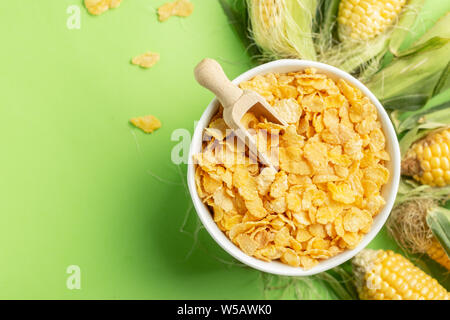 Corn flakes and corn cobs over green background, healthy food concept presentation Stock Photo