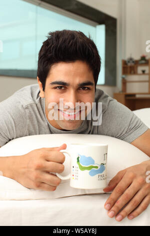 Man having a cup of coffee on bed Stock Photo