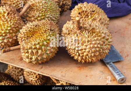 Durian fruits and a knife lay on a counter of marketplace. It is the fruit of several tree species belonging to the genus Durio Stock Photo