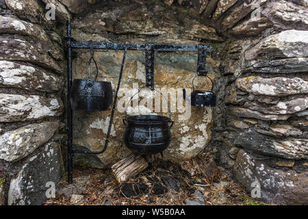 Decorative fireplace with a nostalgic teapot and cooking pots in front of an old stone wall, Ireland Stock Photo