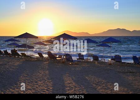 Sunbeds and umbrella on the beach at sunset by the sea. Beautiful concept for vacation, summer holidays and travel.