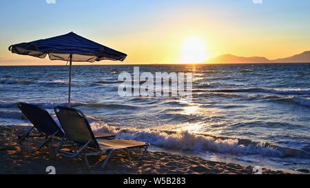 Sunbeds and umbrella on the beach at sunset by the sea. Beautiful concept for vacation, summer holidays and travel. Stock Photo