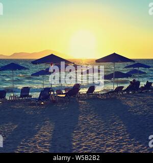 Sunbeds and umbrella on the beach at sunset by the sea. Beautiful concept for vacation, summer holidays and travel. Stock Photo