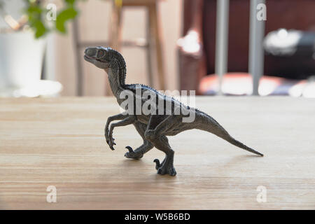 Children's toy ancient predator dinosaur on a wooden table in a room flooded with sunlight. Toy tyrannosaur from plastic. Ancient predatory reptile fr Stock Photo