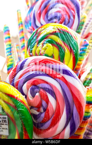 Close up of colorful spiral lollipops wrapped in plastic on display at a candy shop stall with rainbow candy sticks in the background Stock Photo