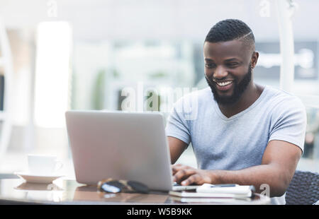 Smiling african man textmessaging on laptop in cafe Stock Photo