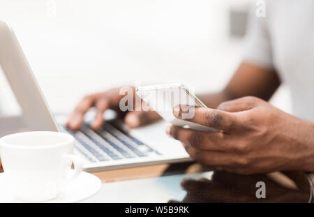 Unrecognizable african man using cellphone and laptop Stock Photo
