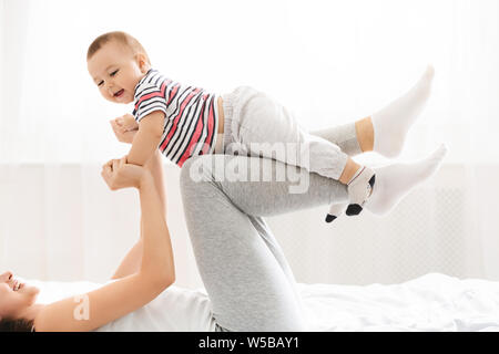 Millennial mommy playing with her baby son, lifting him up on legs Stock Photo