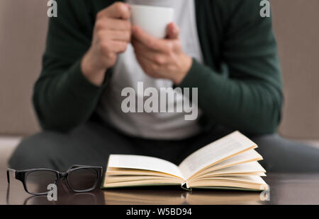 Caucasian man reading book and drinking coffee at home Stock Photo