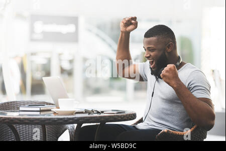 Happy african guy win a lottery online on laptop in cafe Stock Photo