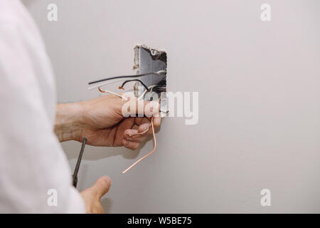 Unfinished electrical mains outlet socket with electrical wires and connector installed in plasterboard drywall is under construction Stock Photo