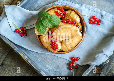 Croissants with currant berries on a wooden tray. The concept of a wholesome breakfast. Stock Photo