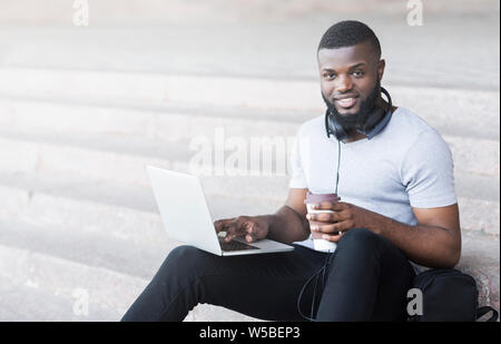 Smiling african student coding outdoor and drinking coffee Stock Photo