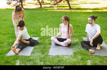 Yoga teacher helping young man to stretch muscles during exercise Stock Photo