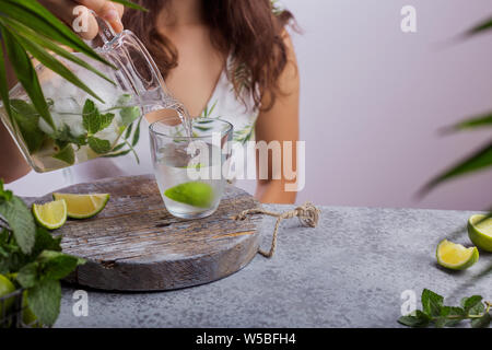 Young woman pouring fresh lemonade from jug into glass Stock Photo