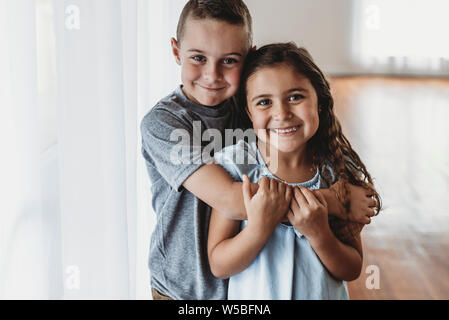 Brother and sister embracing in natural-light studio smiling at camera Stock Photo