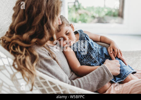 Young girl and mother cuddling on hammock in natural light studio Stock Photo