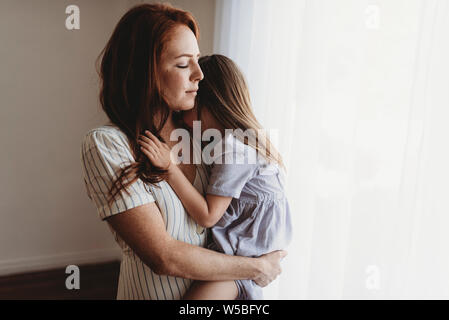 Young mother cuddling with young daughter while closing eyes in studio Stock Photo