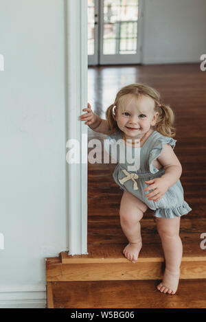 Toddler girl smiling at camera while walking down stairs in a studio Stock Photo